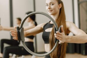 kobieta ubrana w czarny strój do pilatesu ćwicząca z szałwiową obręczą do pilatesu