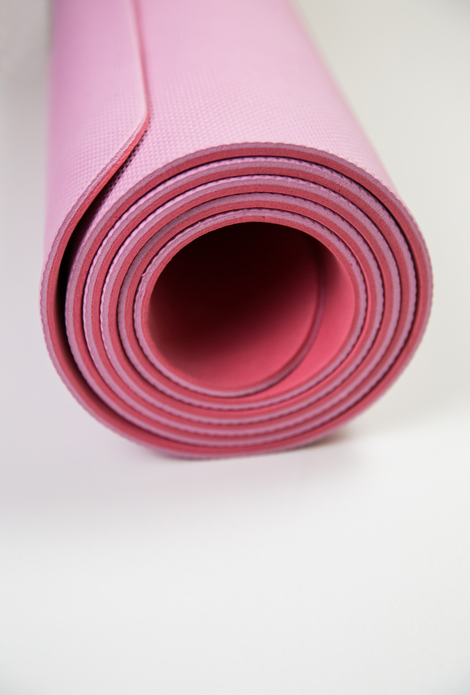 różowa zwinięta mata do pilatesu na białej podłodze