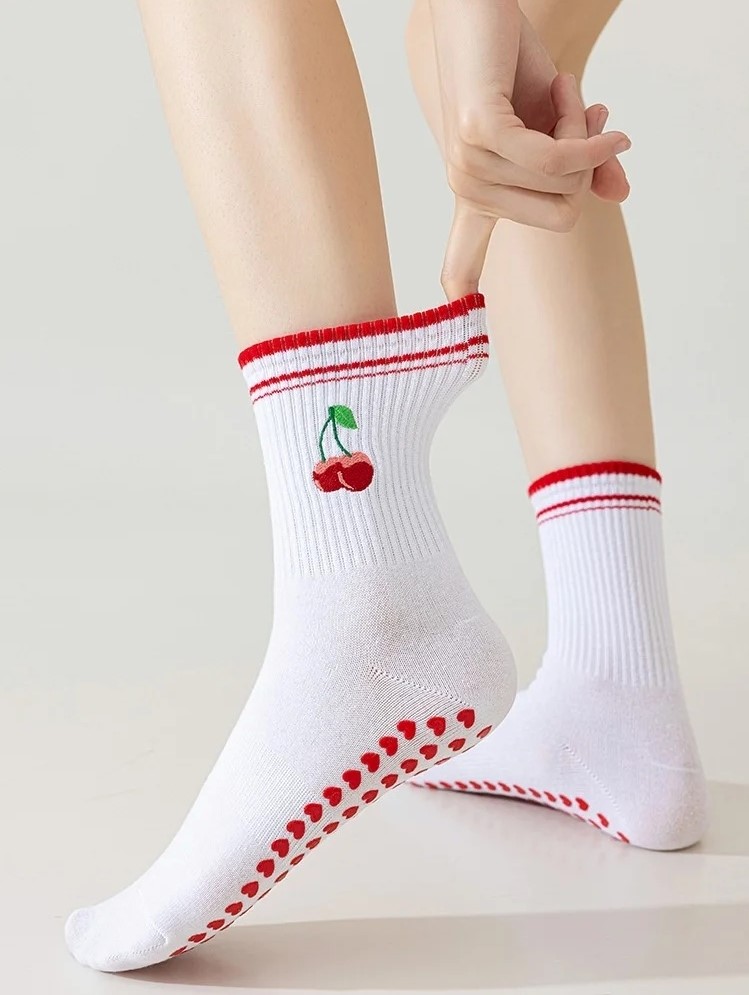 kobieta nosząca retro skarpetki do pilatesu ze wzorem wiśni i trzymająca za ich krawędź